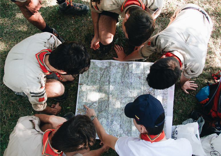 Scouts looking over a map, wearing red and beige scarf around their neck